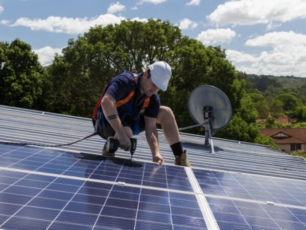 GLS Kredit für Solaranlage auf Firmendach Mann arbeitet auf einem Dach an der Installation einer Photovoltaikanlage.