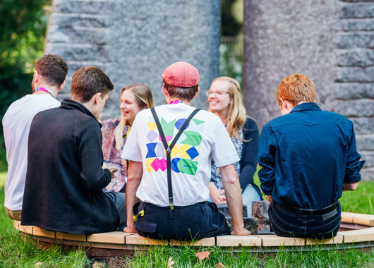 Menschen sitzen auf einer Holzbank im Kreis und unterhalten sich