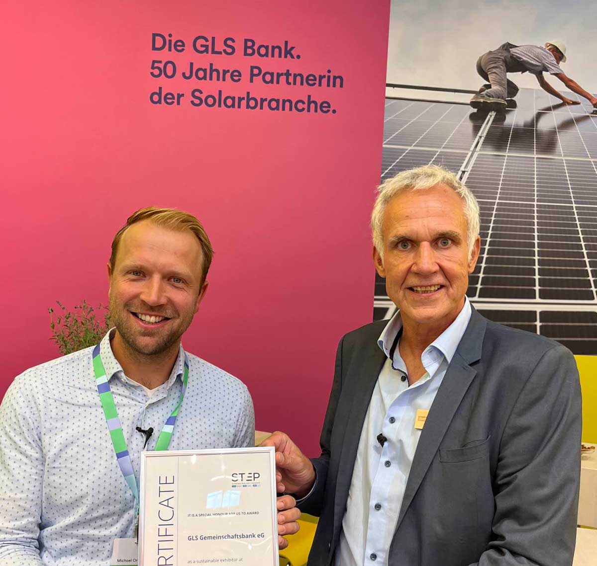 2 männlich gelesen Personen. Michael Orth (links) hält Auszeichnung der Intersolar Messe für den nachhaltigsten Messestand in den Händen