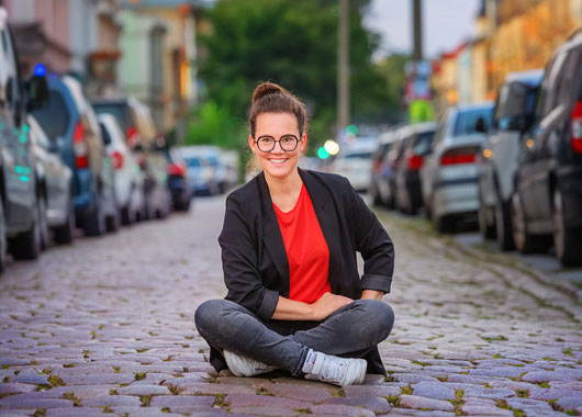Katja Diehl sitzt im Schneidersitz auf einer Straße, rechts und links sind im Hintergrund parkende Autos zu sehen.