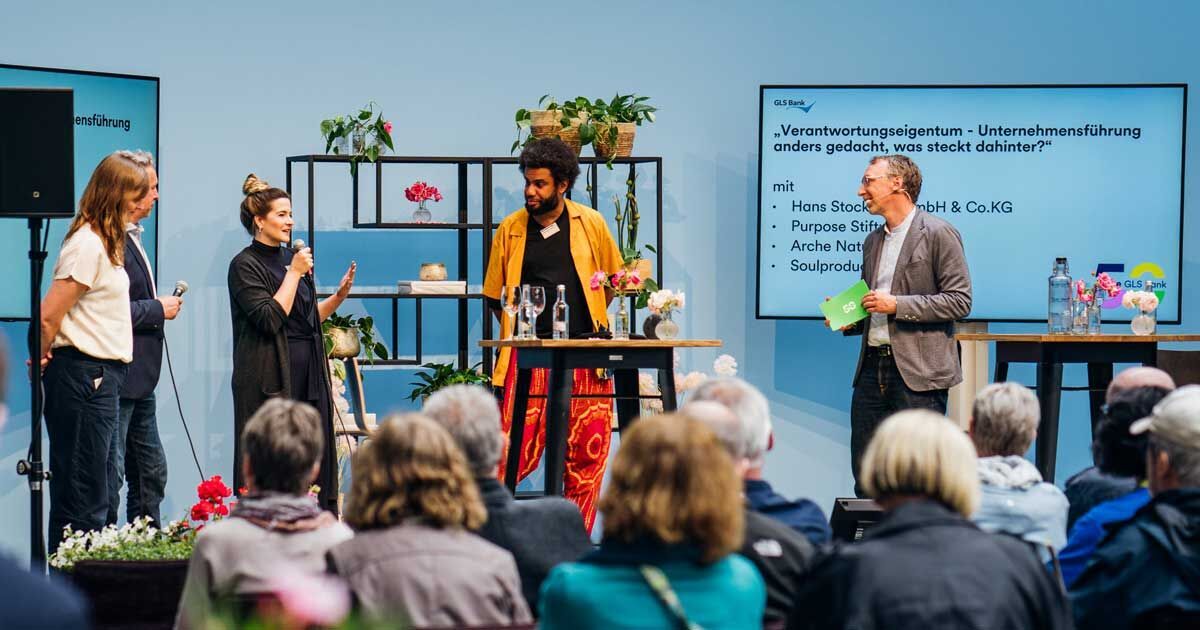 4 Menschen auf der Buehne beim GLS Juilaeumsfestival. Thema: Verantwortungseigentum