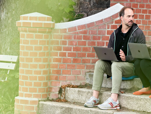 Zwei Menschen mit Laptops sitzen auf einer Eingangstreppe.