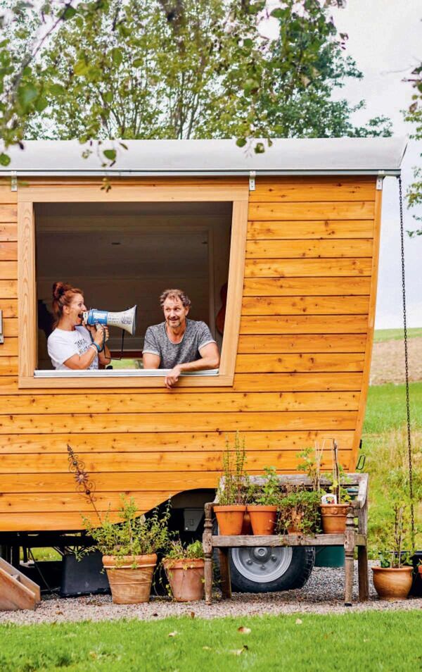 Tinyhouse aus einem Holzwagen mit zwei Menschen die aus dem fenster schauen.