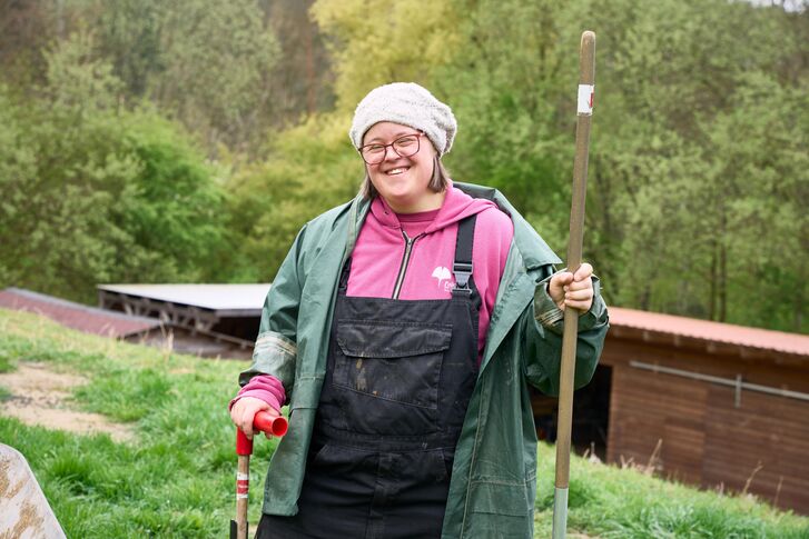 Frau mit Mistgabel in der Hand und Gartenkleidung.