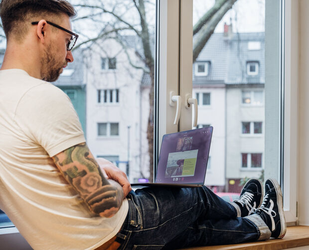 Mann sitzt mit Laptop auf einer Fensterbank in einer Videoberatung.