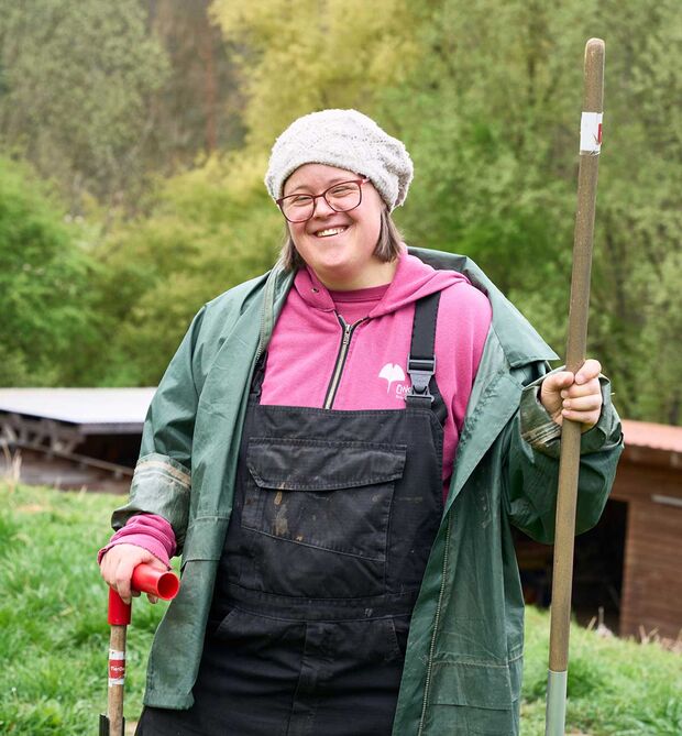 Weiblich gelesene Person steht im Garten und lächelt