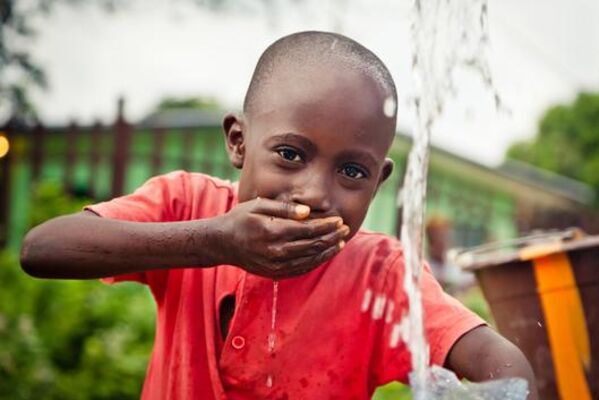 FairWorldFonds investiert in faire Entwicklung Kind schöpft mit der Hand Wasser aus einem Brunnen.