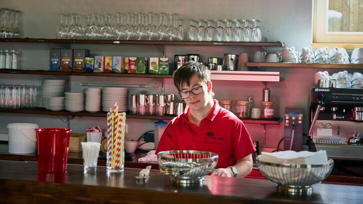 Mensch mit Downsyndrom hinter der Theke eines Cafés