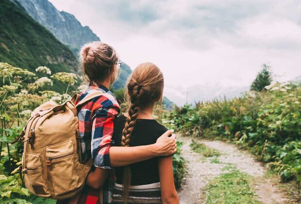 Zwei weiblich gelesene Personen, eine mit Rucksack, schauen auf ein Bergpanorama