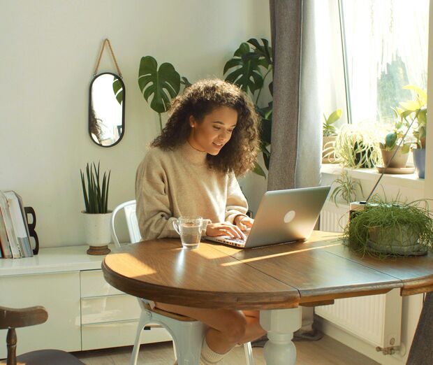 Frau am Tisch mit Laptop und Tee, Pflanzen im Hintergrund