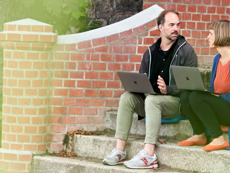 Eine Frau und ein Mann sitzen auf einer Außentreppe mit Laptops.