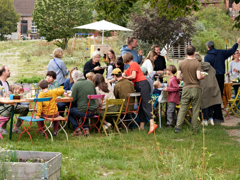 Menschengruppe an langer bunter Tafel in einem Garten.