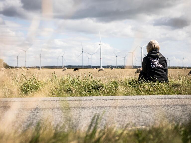 Frau sitzt auf einem Feld vor einem Windpark