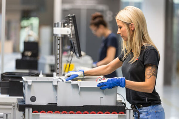 Frau mit Arbeitshandschuhen arbeitet an einem Fließband.