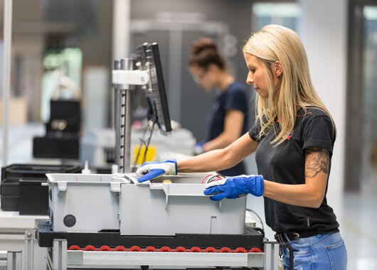 Frau mit Arbeitshandschuhen arbeitet an einem Fließband.