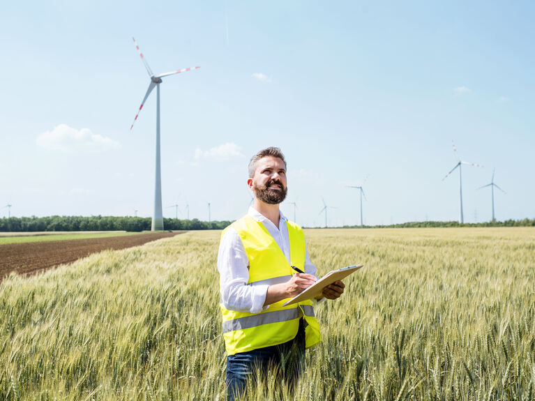 Mann mit Schutzweste auf einem Feld vor Windkraftanlagen